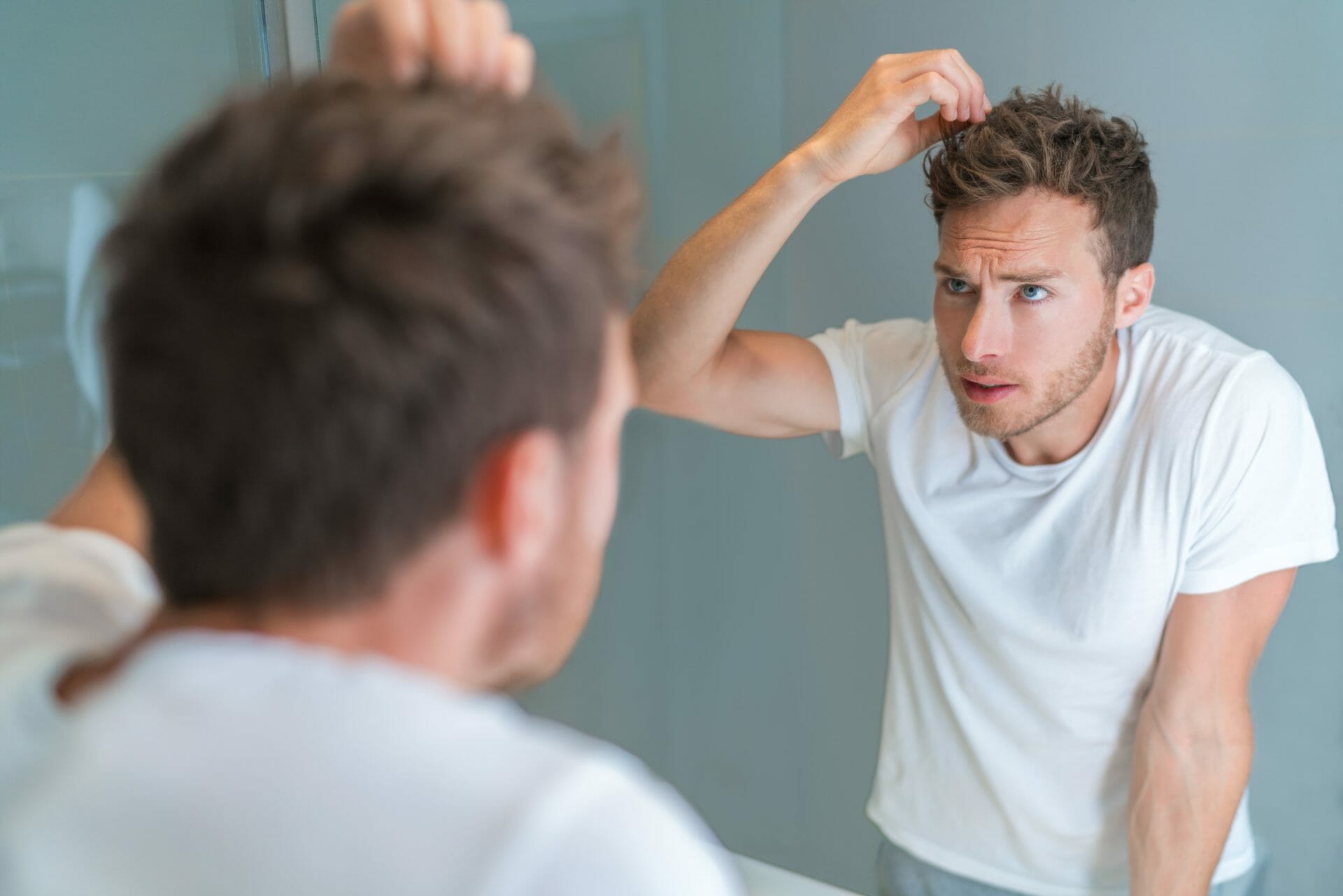 man looking in bathroom mirror styling hairstyle with gel or checking for hair loss or grey hairs