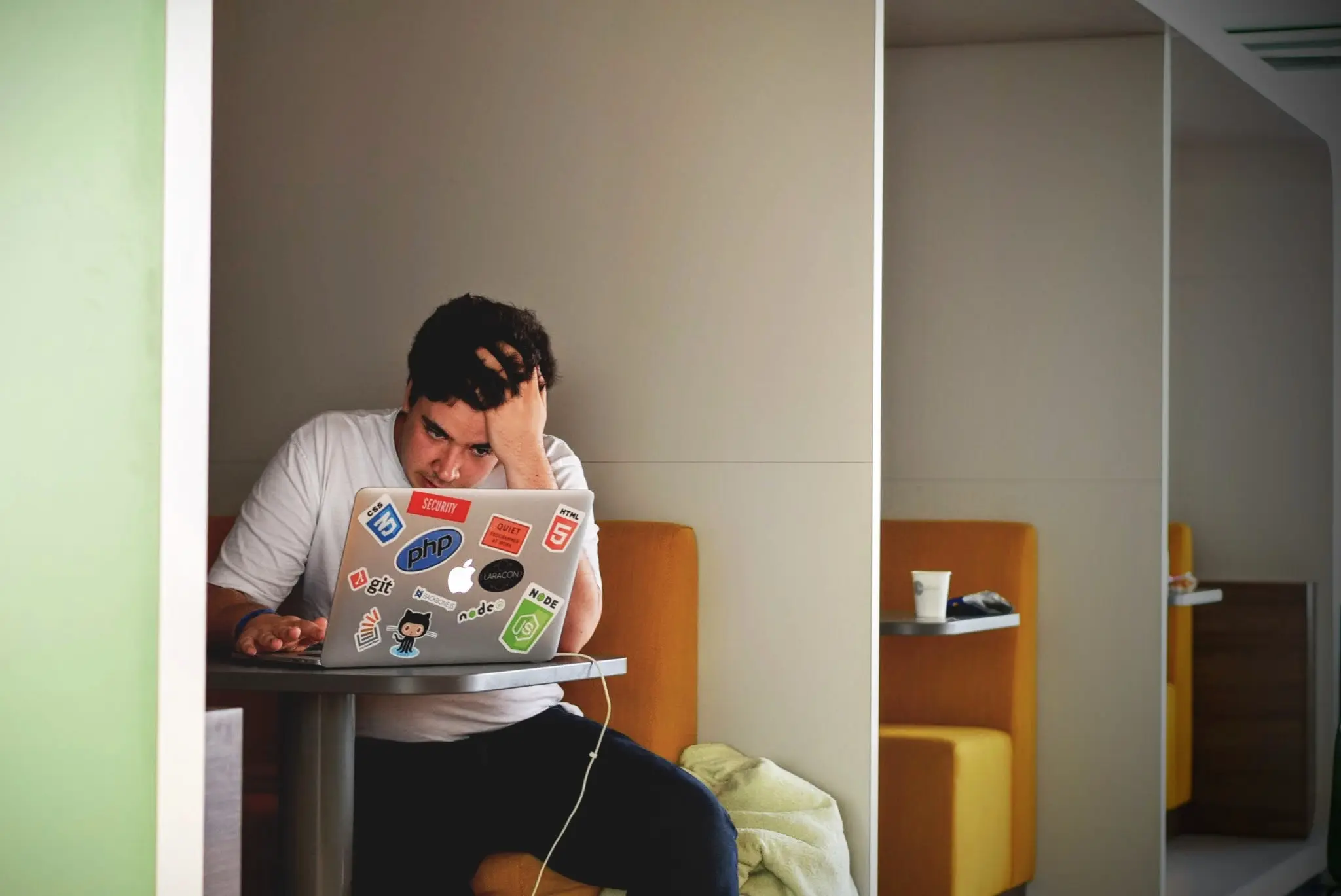 a stressed man with hair loss using a laptop in a booth with yellow seats